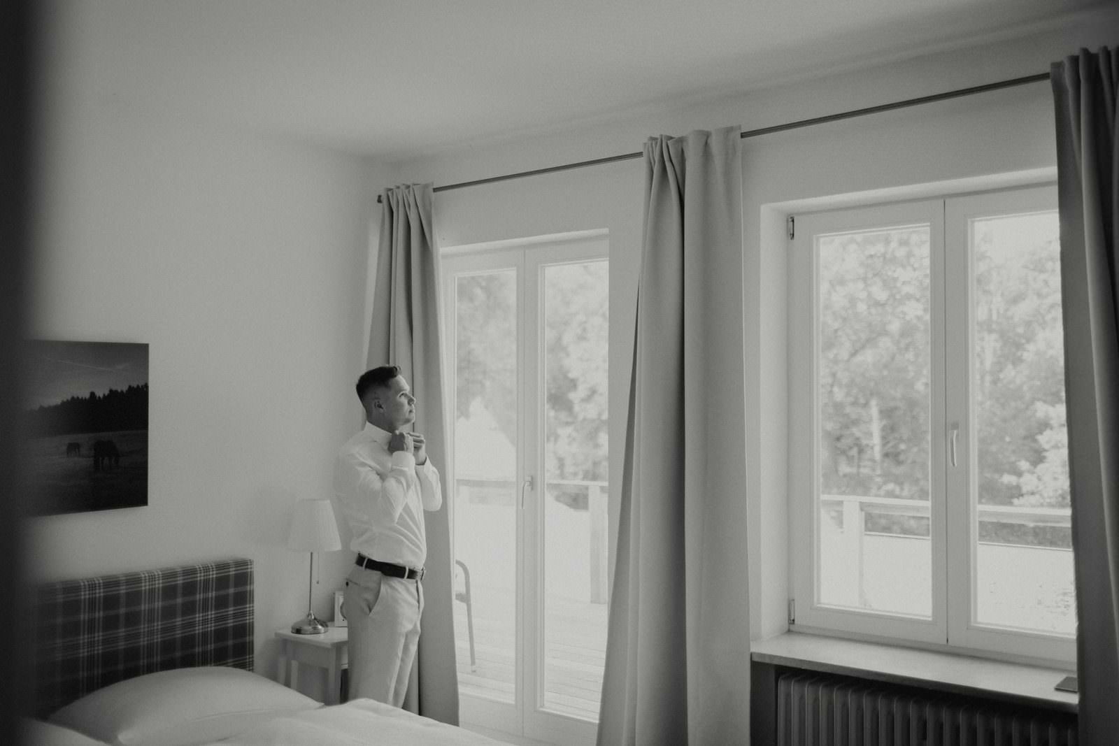 Basti am Fenster: Fliege binden, Schwarzweiß, Hotelzimmer mit Ausblick in den Park.