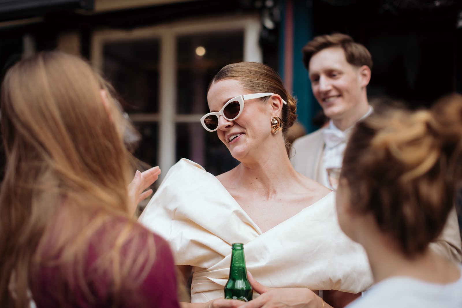 Jana lacht mit Gästen, Sonnenbrille im Haar